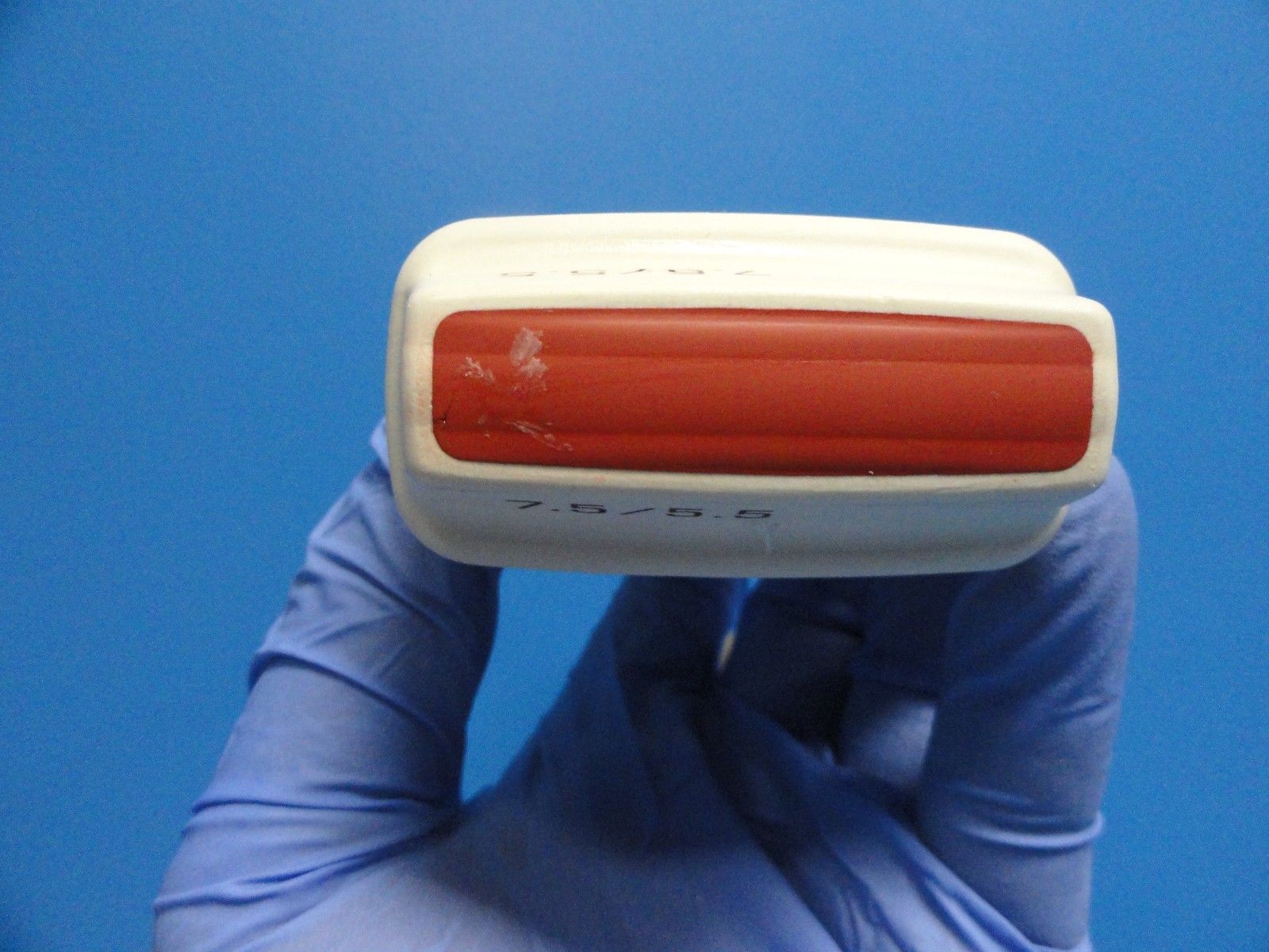 a hand in a glove holding a red and white device